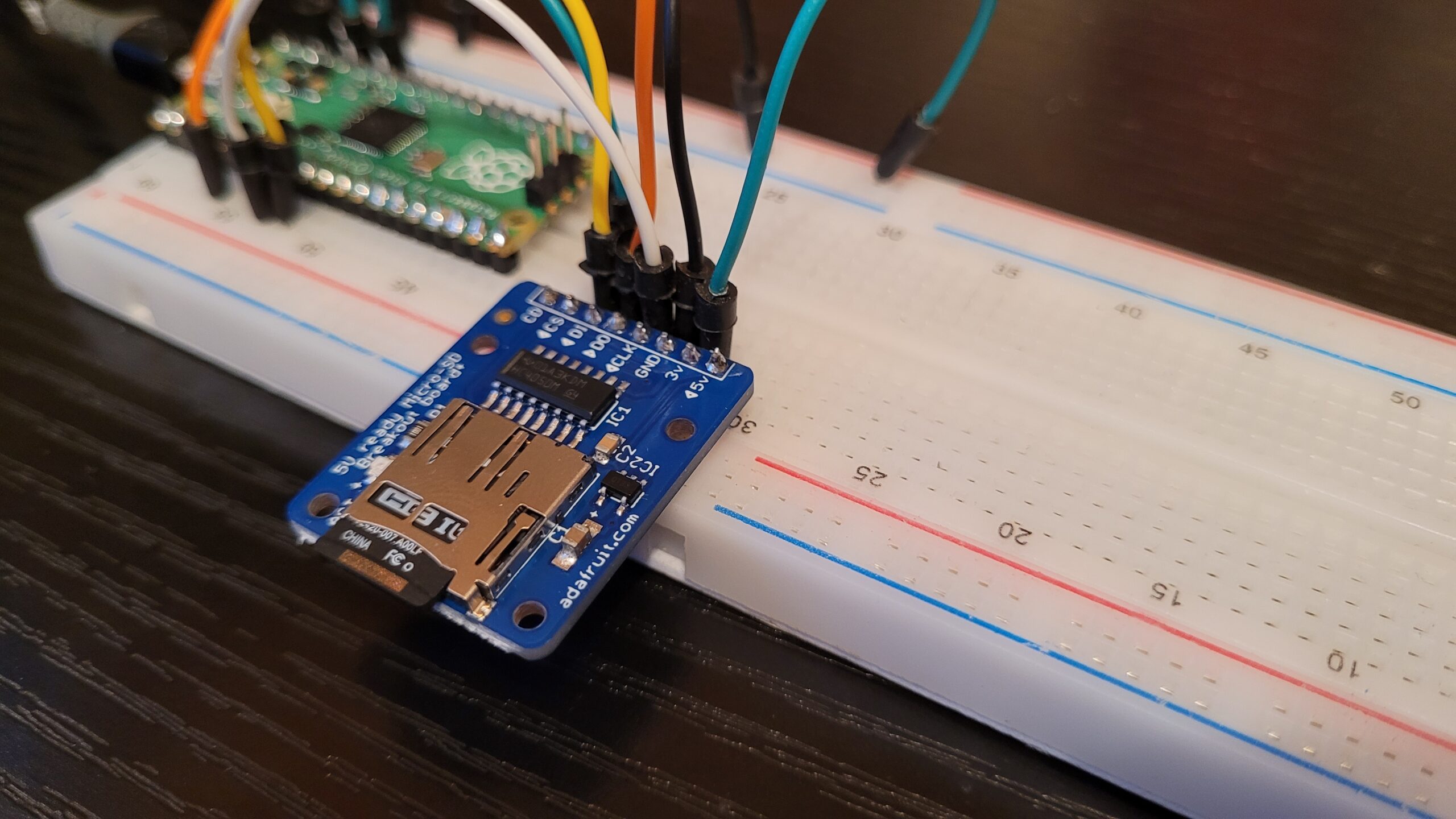 A photograph of a MicroSD breakout module, connected to a solderless breadboard. A Raspberry Pico is also connected to the breadboard, but is out of focus.